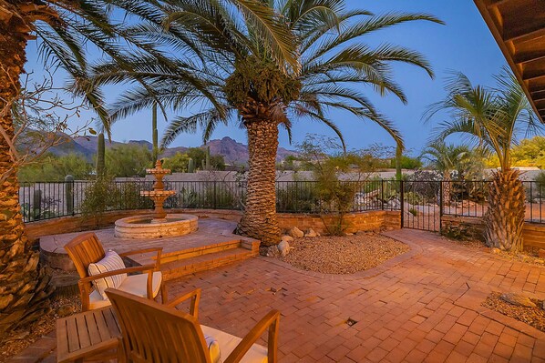 An outdoor patio with a fountain, palm trees, and a view of mountains.