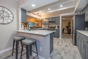 A modern kitchen with a central island, bar stools, and a clock on the wall.