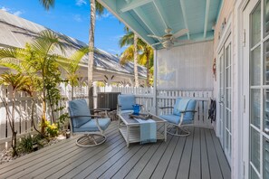 A covered outdoor deck with white railings, blue chairs, and a table with a blue cushion.