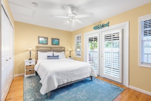 A bedroom with a bed, nightstands, a ceiling fan, and a view through the window blinds.
