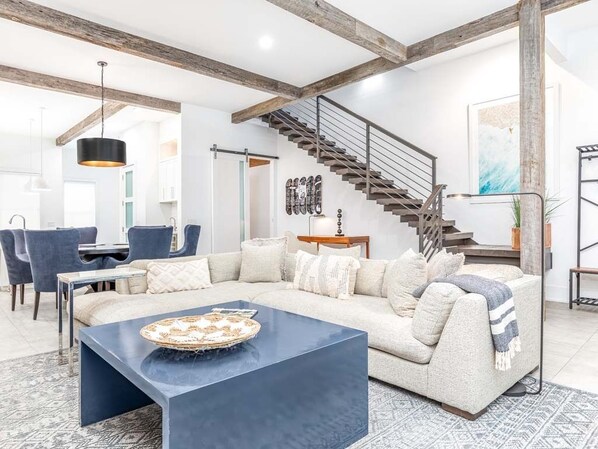 Uma sala de estar moderna com um sofá modular, uma mesa de centro escura e uma escada com corrimão de metal.