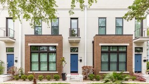 A row of modern townhouses with brick facades, large windows, and a well-maintained front yard with hedges and small plants. - Savannah Jetsetter | Pet Friendly, Luxury Townhome, Historic Savannah (Savannah)