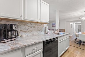 A modern kitchen with white cabinets, a marble countertop, a coffee maker, and a dishwasher.