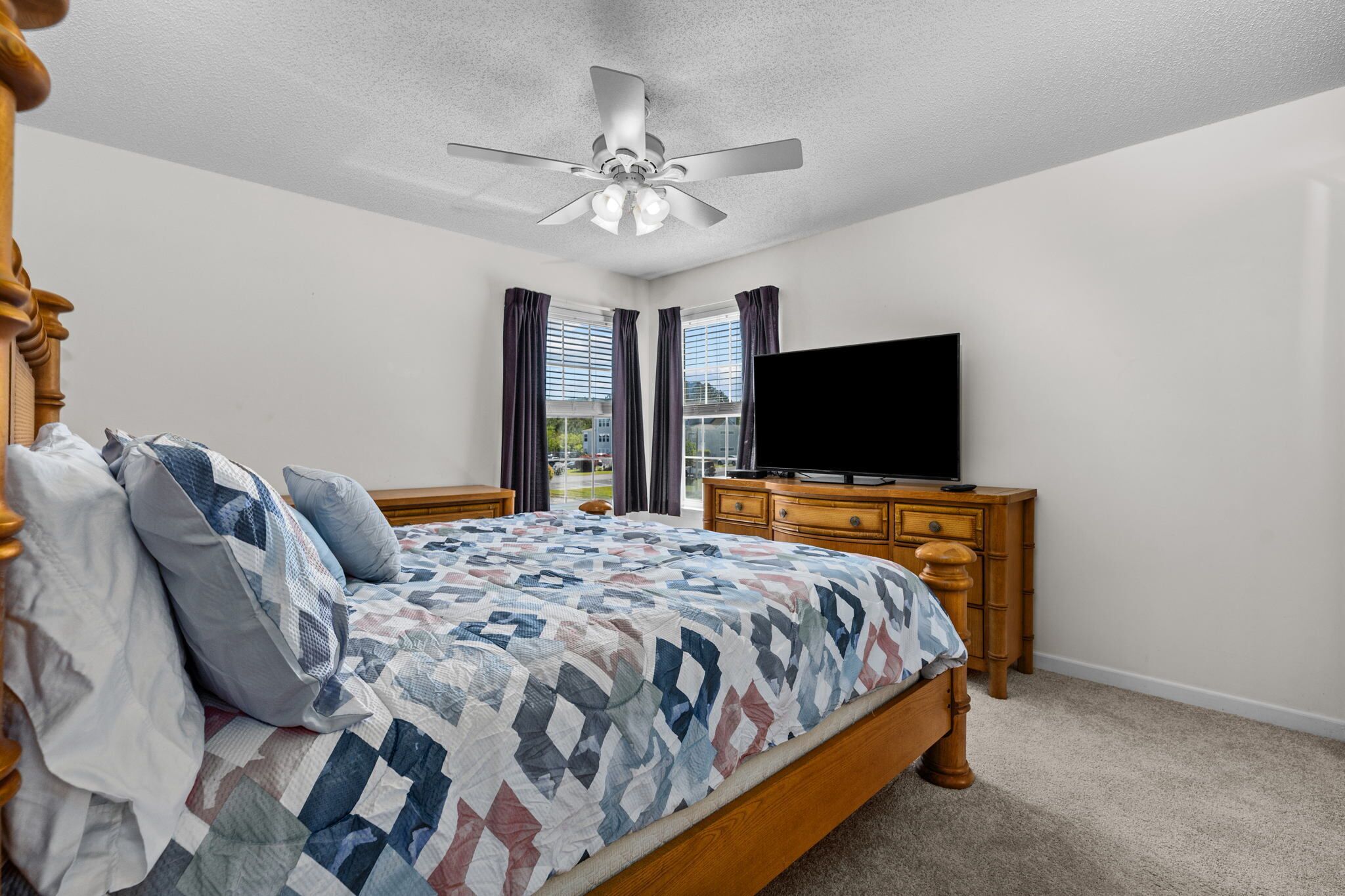 Une chambre à coucher avec un lit, un ventilateur de plafond, une commode et un téléviseur.