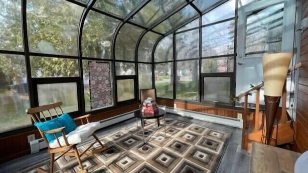 Un invernadero con suelo de patrón geométrico, muebles de madera y grandes ventanas que ofrecen vistas al exterior.