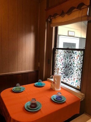 Ein Essbereich mit einer holzverkleideten Wand, einem Fenster mit floralem Muster und einem Tisch, gedeckt mit Tellern und einer Kanne.