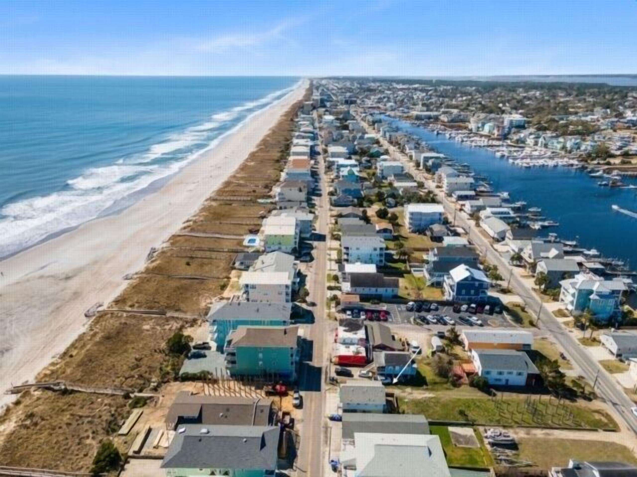 Zona residencial costera con casas a lo largo de la playa y un puerto deportivo.
