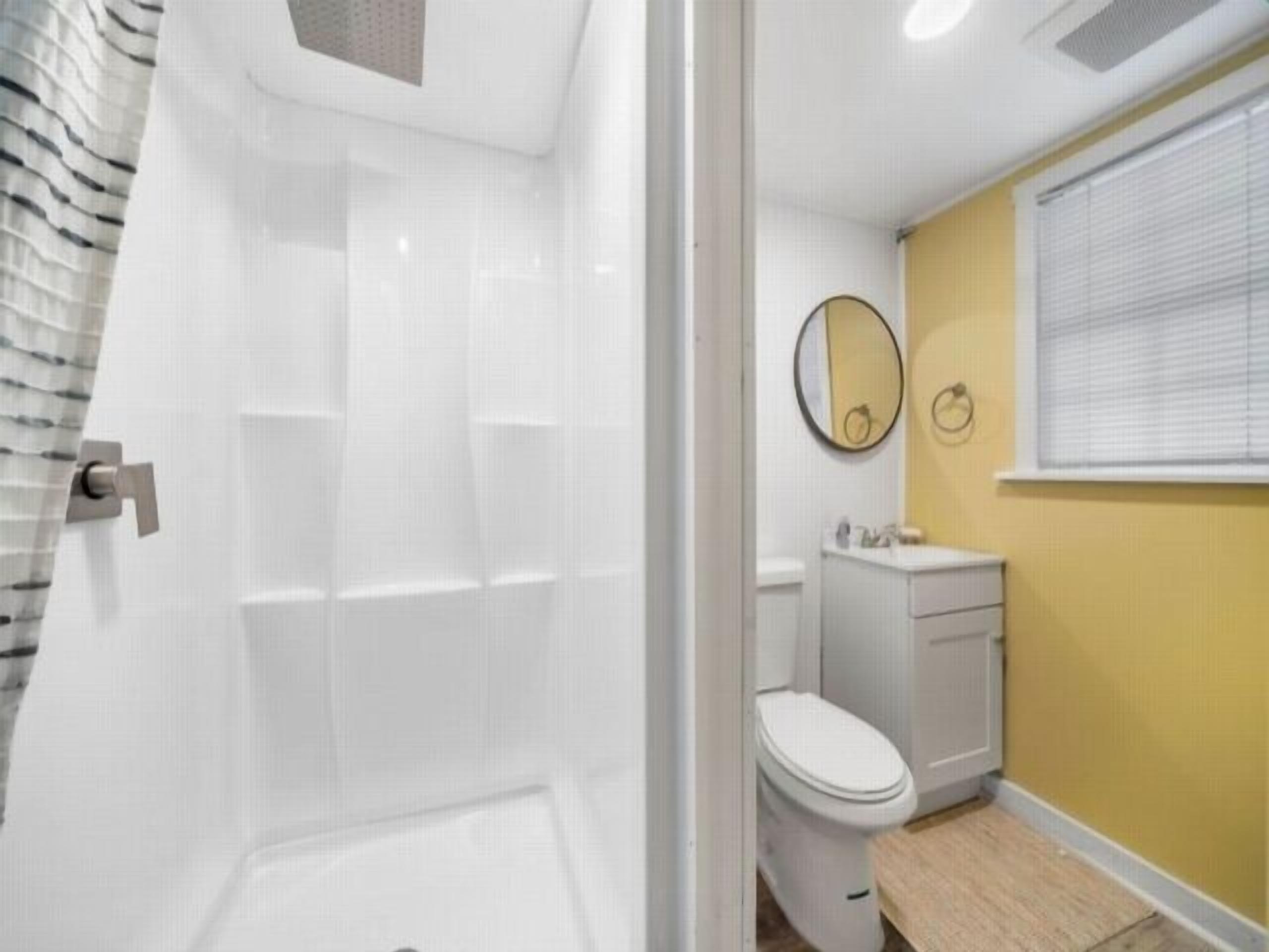 Un baño con cabina de ducha blanca, inodoro y lavabo con espejo.