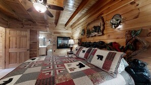 A log cabin bedroom with a large bed, wooden walls, a ceiling fan, and a fireplace.