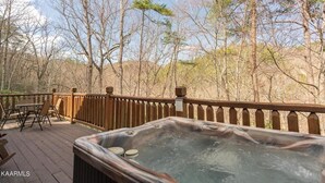 A hot tub on a wooden deck with a view of trees and hills.