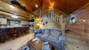 A wooden cabin interior with a living area, kitchen, and a staircase.