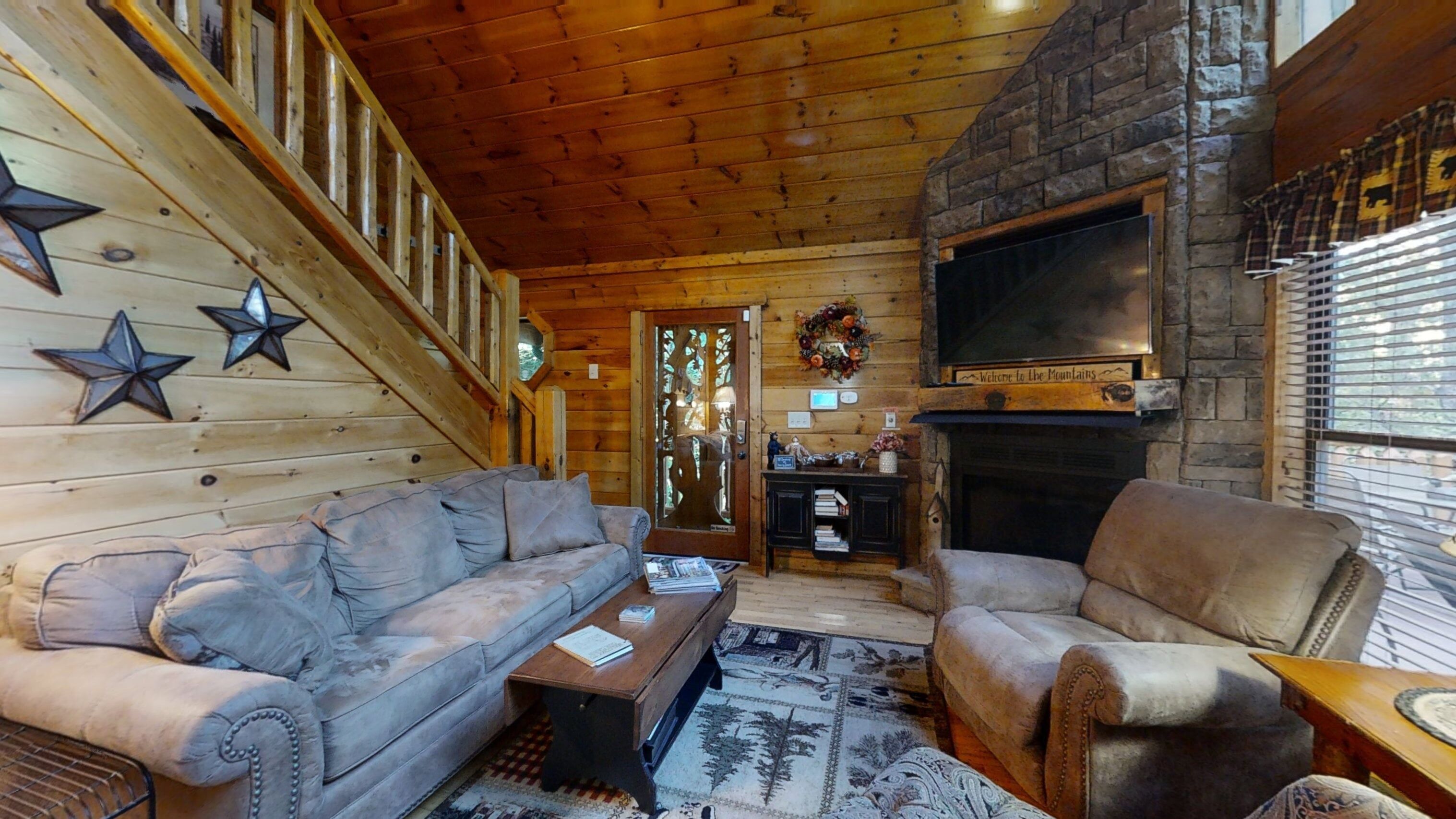 A cozy log cabin interior with a wooden staircase, a fireplace, and a television mounted above it.