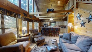 A cozy cabin interior with a living room, kitchen, and a loft area.
