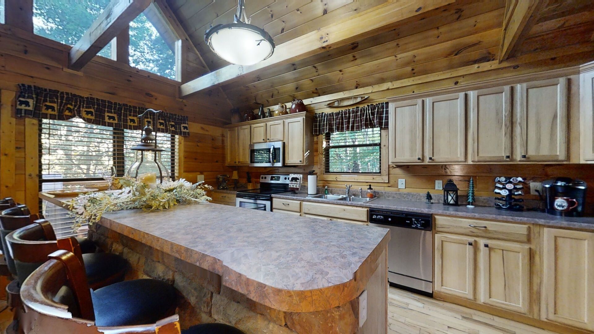 L’intérieur d’une cabane en bois, avec un îlot central en pierre, des armoires en bois et une grande fenêtre.
