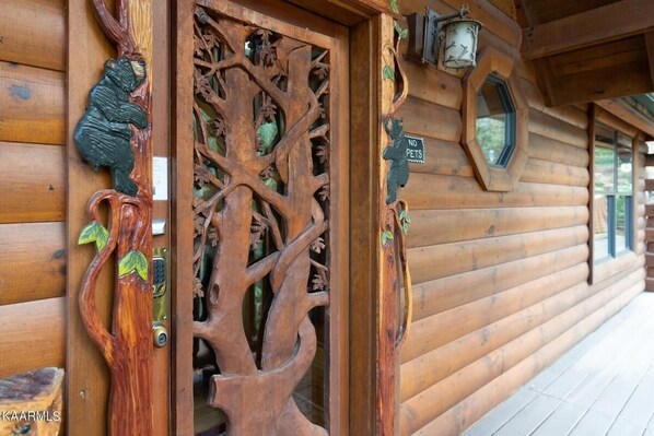 A wooden cabin with a carved tree door, a 'No Pets' sign, and a circular window.
