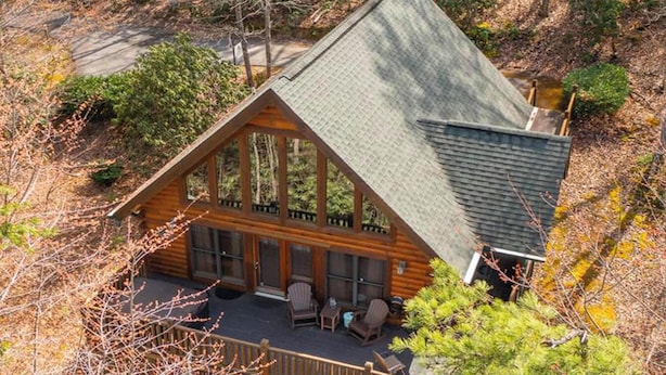 A cabin with a large porch, multiple windows, and a sloped roof.