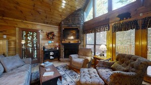 A cozy cabin interior with a stone fireplace, wooden walls, and a large window. - Wuzzy's Flophouse 2 Bedroom Cabin by RedAwning (Sevierville)
