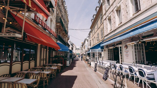 Une rue étroite bordée de cafés et de restaurants, avec des terrasses et une grande variété de styles architecturaux.