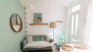 Une pièce chaleureuse avec un canapé gris, une petite table surmontée de sets de table en fibres tressées, une lampe, un tableau encadré au mur et une fenêtre avec des rideaux.
