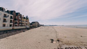 Une plage bordée d’une rangée d’immeubles à plusieurs étages dotés de balcons, une plage de sable et un ciel dégagé.