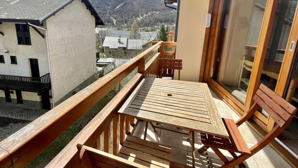 A balcony with a wooden table and chairs, a glass door, and a view of snow-capped mountains. - Balcony & serenity: peak views (Le Monêtier-les-Bains)