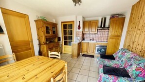 A compact kitchen with wooden cabinets, a dining table with chairs, and a sofa with a colorful blanket. - Balcony & serenity: peak views (Le Monêtier-les-Bains)
