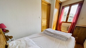 A neatly made bed with white linens, a wooden headboard, a red lamp, and a window with curtains. - Balcony & serenity: peak views (Le Monêtier-les-Bains)
