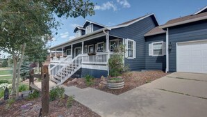 A two-story house with a covered porch, a front garage, and a landscaped front yard. - Upper Unit: Raspberry Mountain Family Farmhouse (Monument)