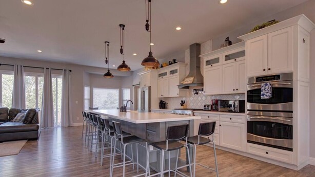 A modern kitchen with white cabinetry, a central island with bar stools, stainless steel appliances, and pendant lighting. - Upper Unit: Raspberry Mountain Family Farmhouse (Monument)