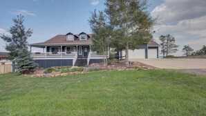 A two-story house with a covered front porch, a small front yard with a tree, and a garage. - Upper Unit: Raspberry Mountain Family Farmhouse (Monument)