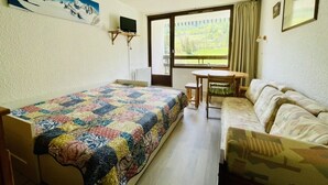 A bedroom with a bed, a sofa, a table, and a chair. There is a window with a view of greenery outside. - Nice 28m² Comfort In The Heart La Salle Les Alpes (La Salle-les-Alpes)