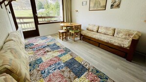 A cozy room with a bed, a colorful quilt, a sofa, a small table, and chairs. There is a window with a view of greenery outside. - Nice 28m² Comfort In The Heart La Salle Les Alpes (La Salle-les-Alpes)
