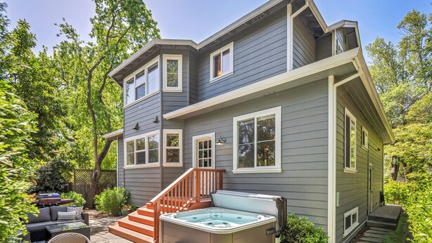Una casa de dos pisos con un jacuzzi, mobiliario exterior y una escalera que conduce al nivel superior.