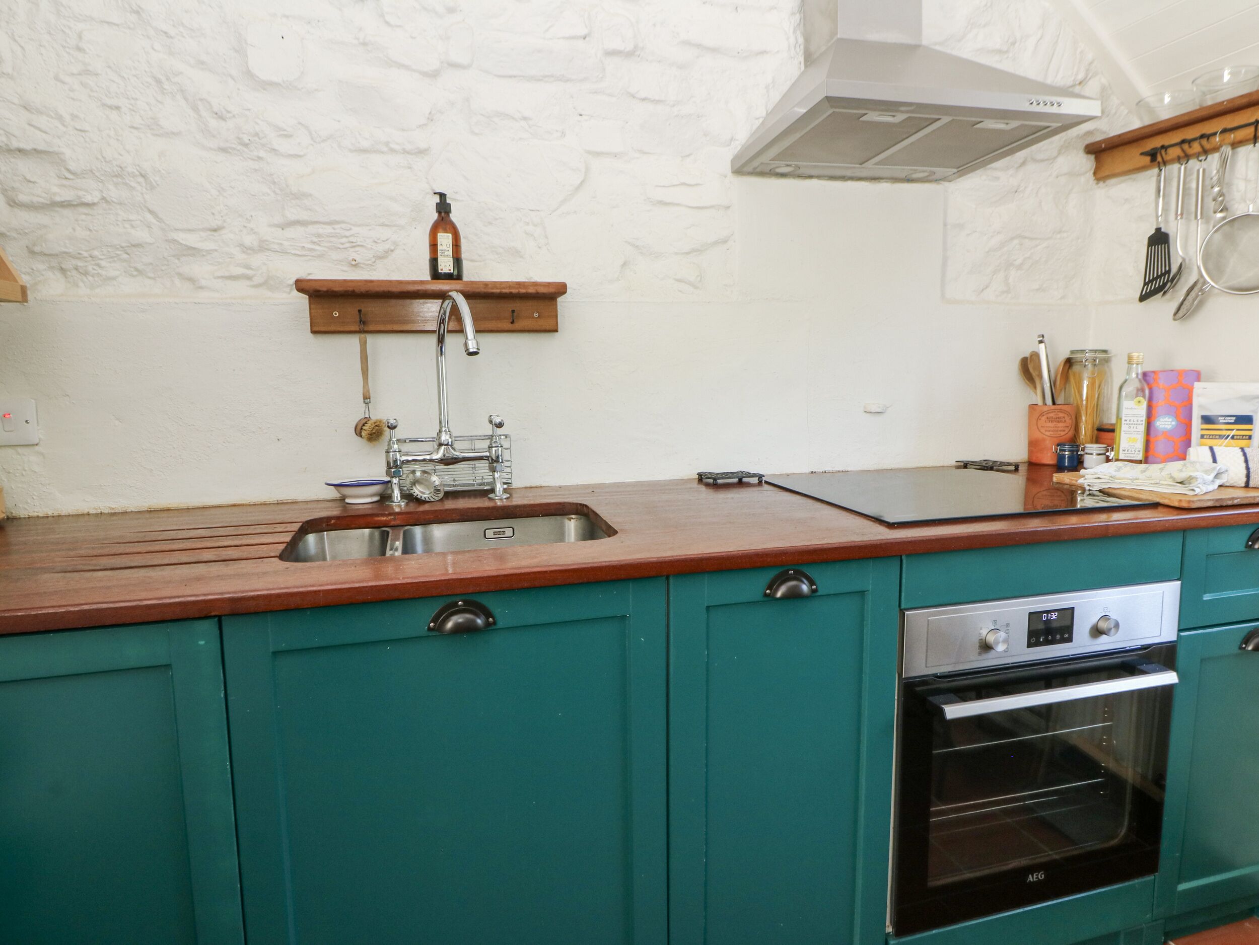 Una cocina con armarios color turquesa, un lavamanos de acero inoxidable, encimera de madera y horno empotrado.