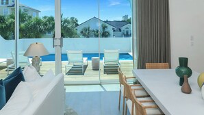 Habitación moderna con vista a la piscina, muebles blancos y zona de comedor con sillas de mimbre.