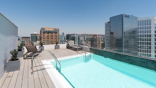 Una piscina en la azotea con vista a la ciudad, sillas de descanso y una terraza de madera.