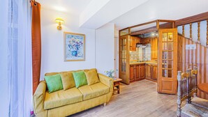 Un salon avec un canapé jaune, un escalier en bois et un coin cuisine.