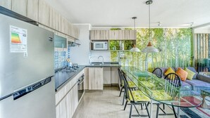 A modern kitchen with a glass dining table, wooden cabinets, and a view of greenery through a glass wall. - Blue Oasis 2BR W/ Pool, Parking & Gym (Viña del Mar)