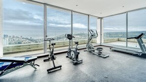 A gym with various exercise equipment and large windows offering a city view. - Blue Oasis 2BR W/ Pool, Parking & Gym (Viña del Mar)