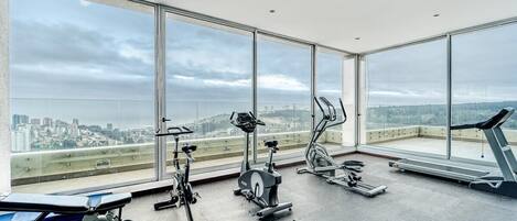 A gym with various exercise equipment and large windows offering a city view.