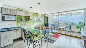 A modern kitchen with a glass dining table and chairs, a microwave, and a view of the city through large windows. - Blue Oasis 2BR W/ Pool, Parking & Gym (Viña del Mar)