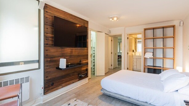 A modern bedroom with a large bed, a wooden accent wall, a built-in TV, and a walk-in closet.