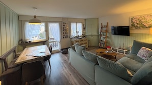 Ein gemütliches Wohnzimmer mit einer Couch, einem Esstisch und einem an der Wand befestigten Fernseher.