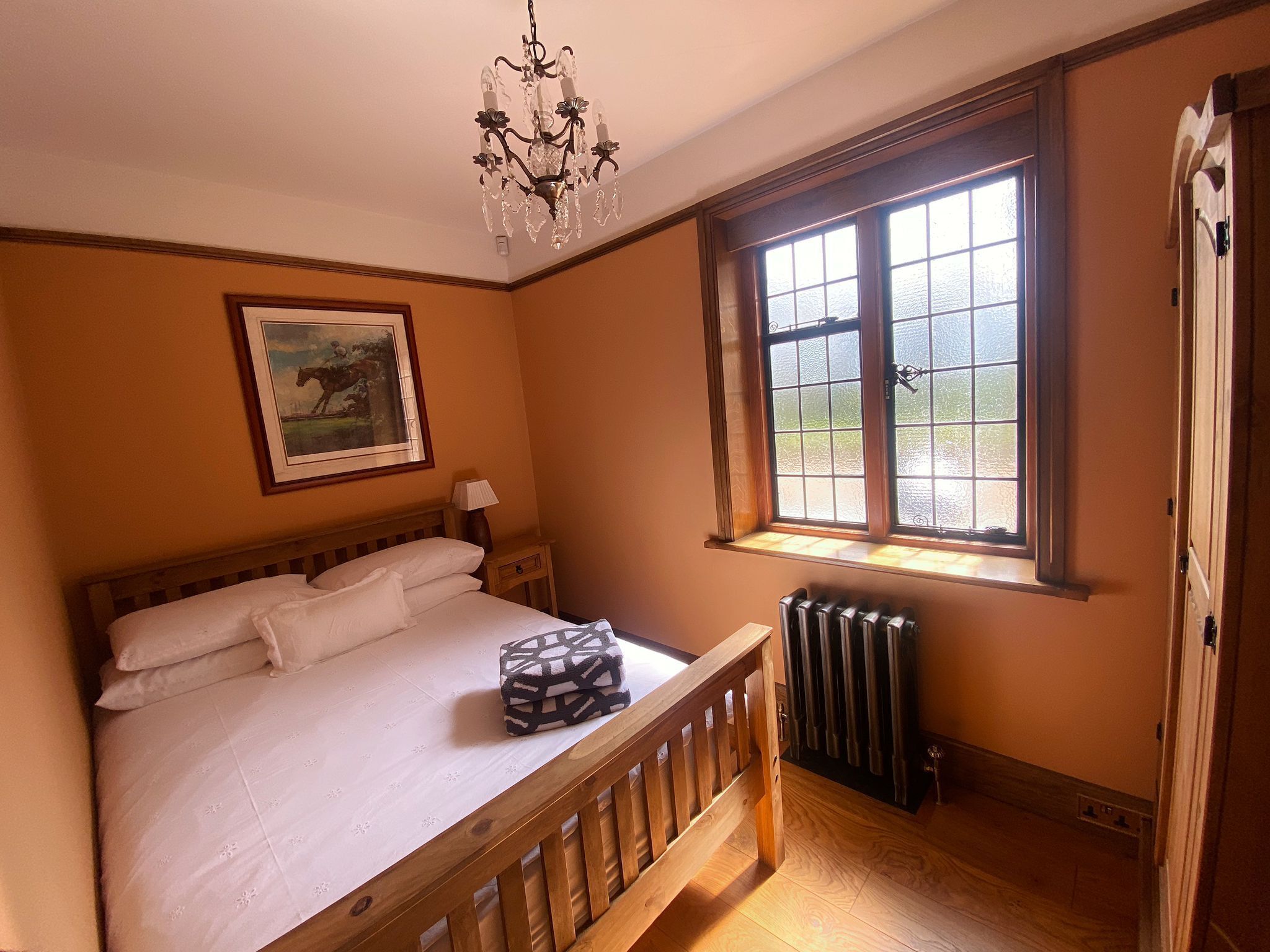 Une chambre avec un lit en bois, un radiateur, une fenêtre donnant sur un beau paysage et un lustre.