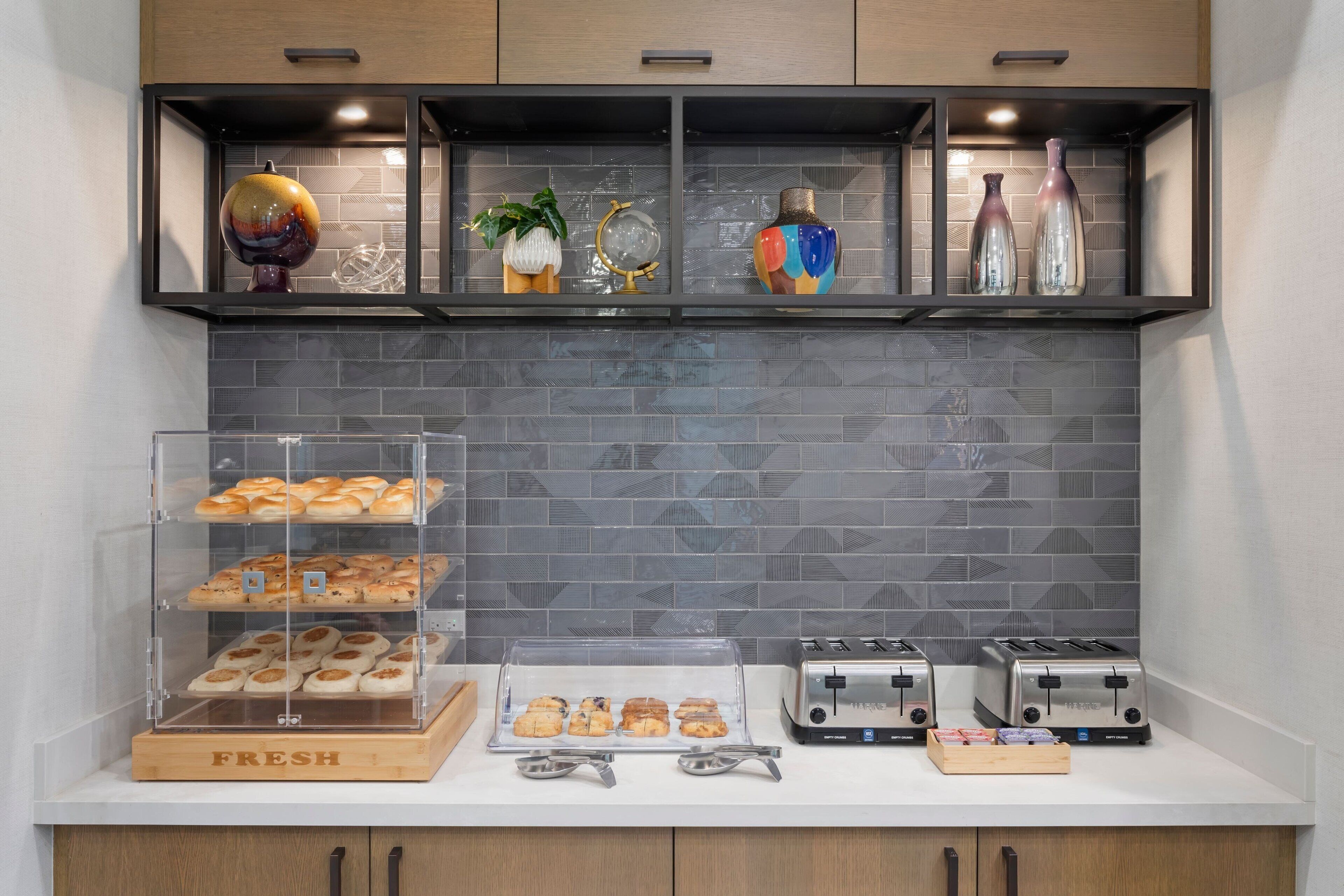 A kitchen counter with a bread display, two toasters, and a decorative shelf with various items.