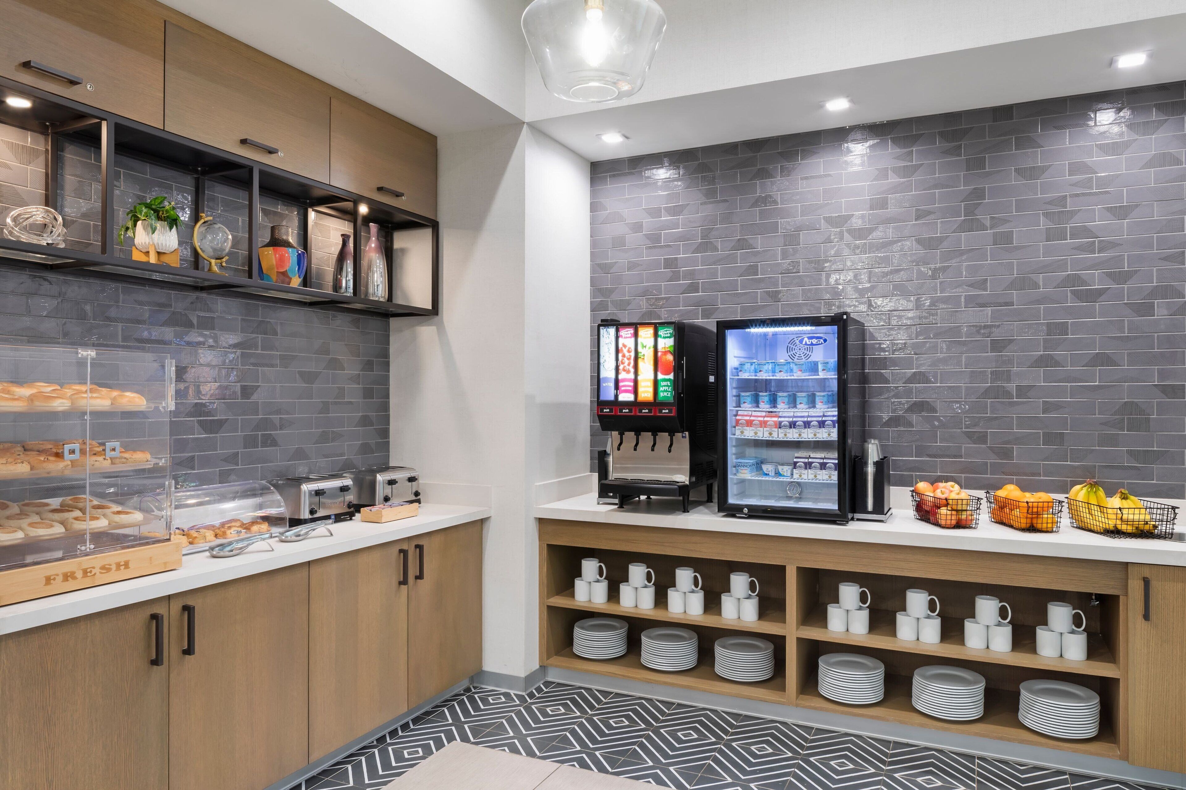 Una kitchenette moderna con una cafetera, un dispensador de bebidas y un refrigerador lleno de bebidas.