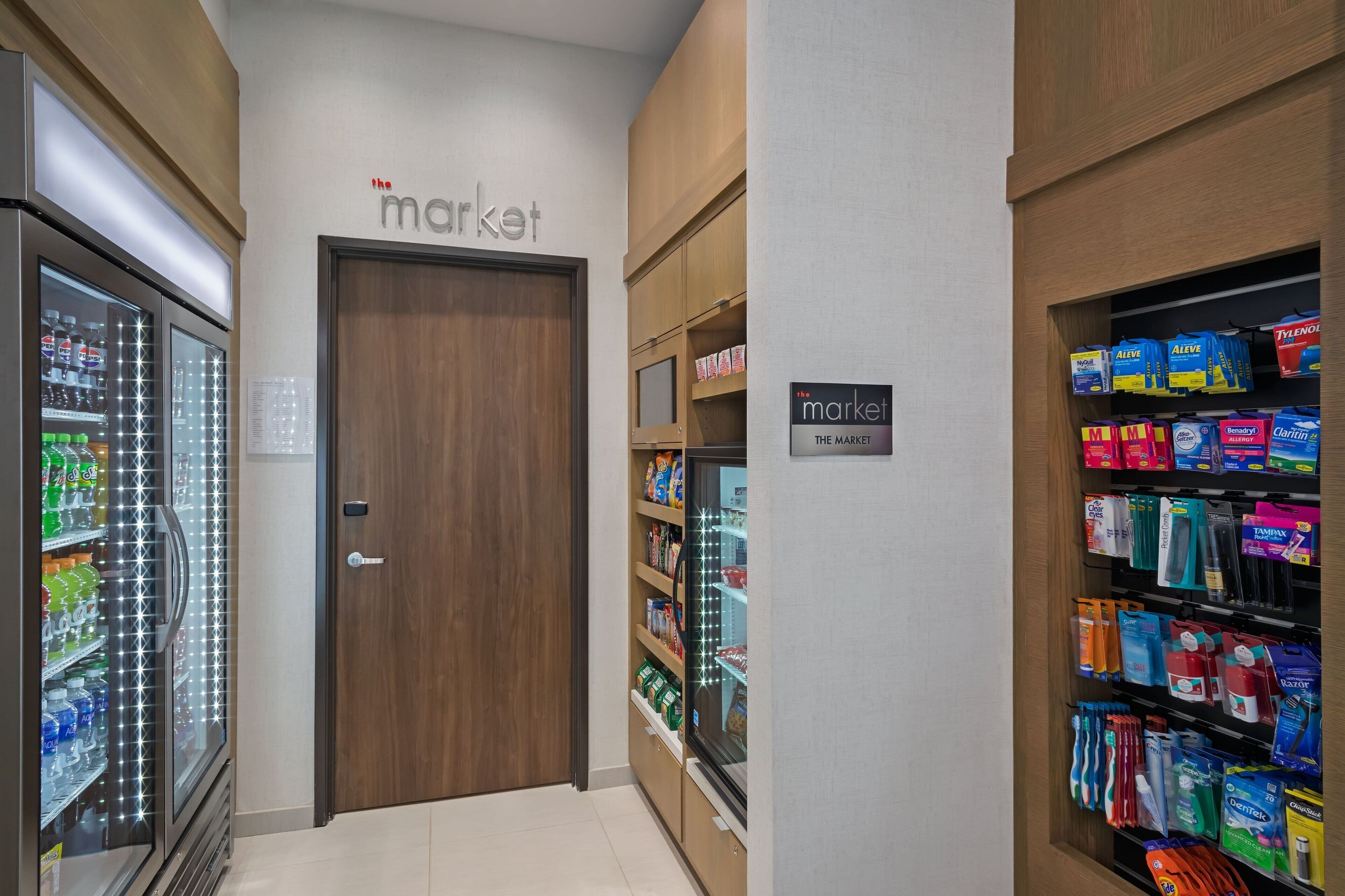 Interior de una tienda con una puerta de madera que indica 'market', dispensadores refrigerados de bebidas y estantes repletos de diversos productos.