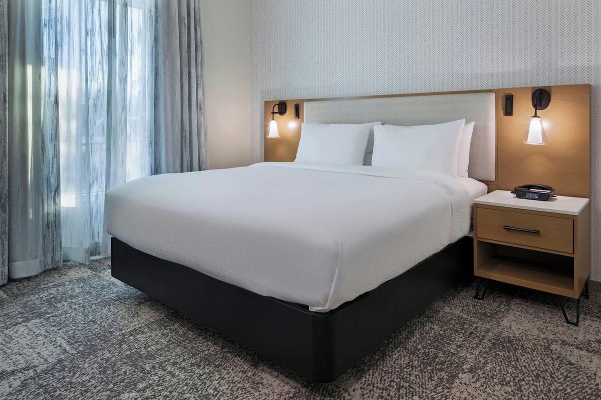 A hotel room with a large bed, a bedside table with a lamp, and a nightstand.
