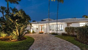 Una casa moderna con entrada de ladrillo, puerta de vidrio y palmeras.