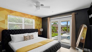 Un dormitorio con una cama grande, ventilador de techo, puerta corredera de vidrio a un área de piscina y un espejo.